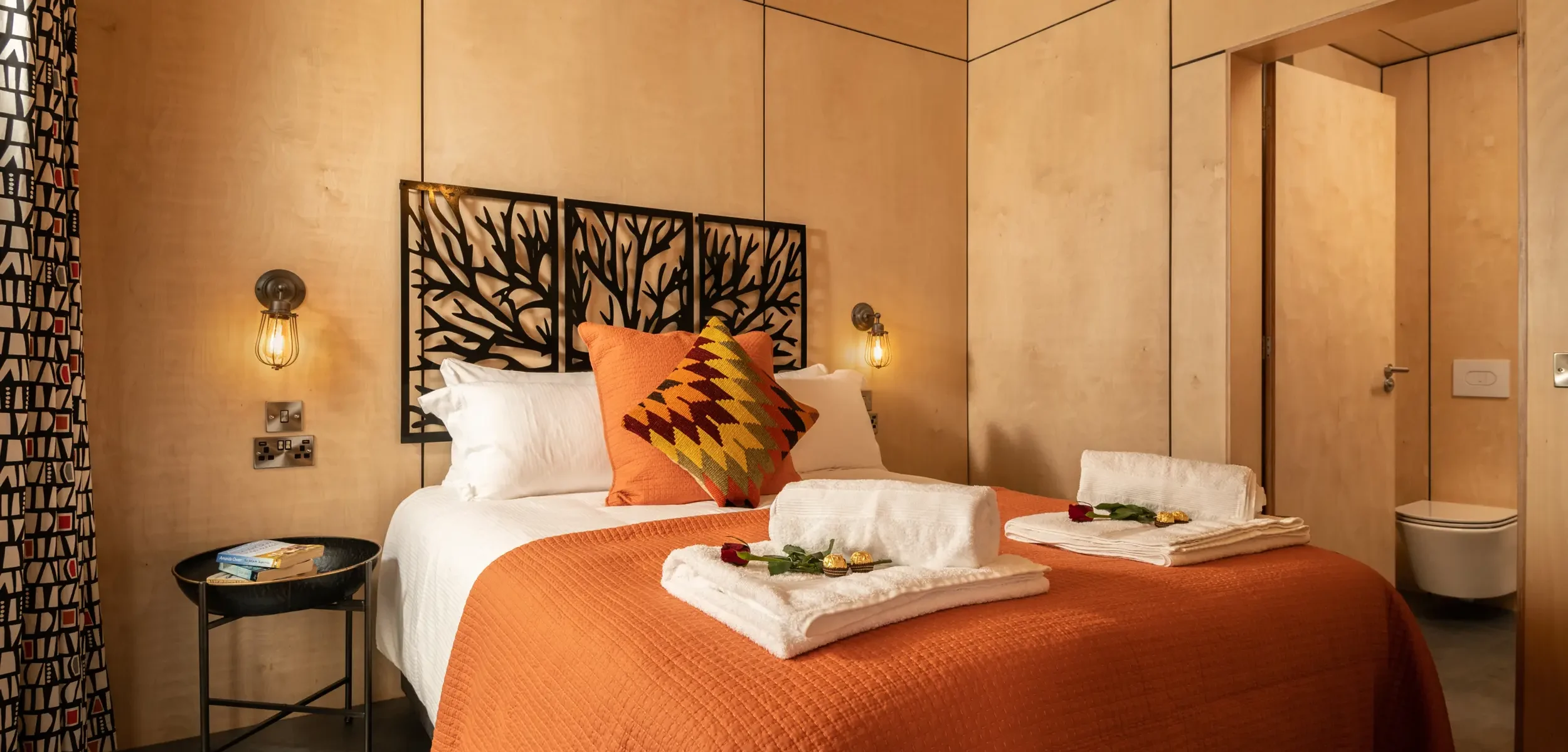 Industrial-chic bedroom with warm burnt orange tones and locally made metal headboard at Peregrine Retreat