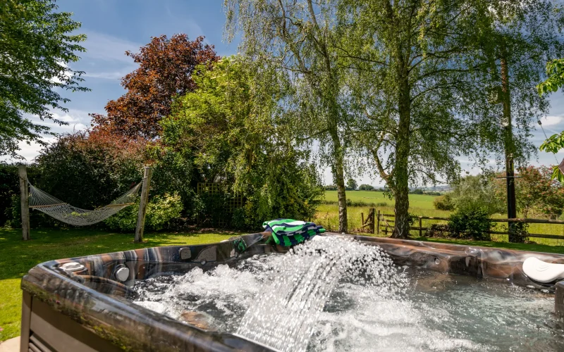 Hot tub in the foreground with garden hammock and countryside views beyond at Old Barn House