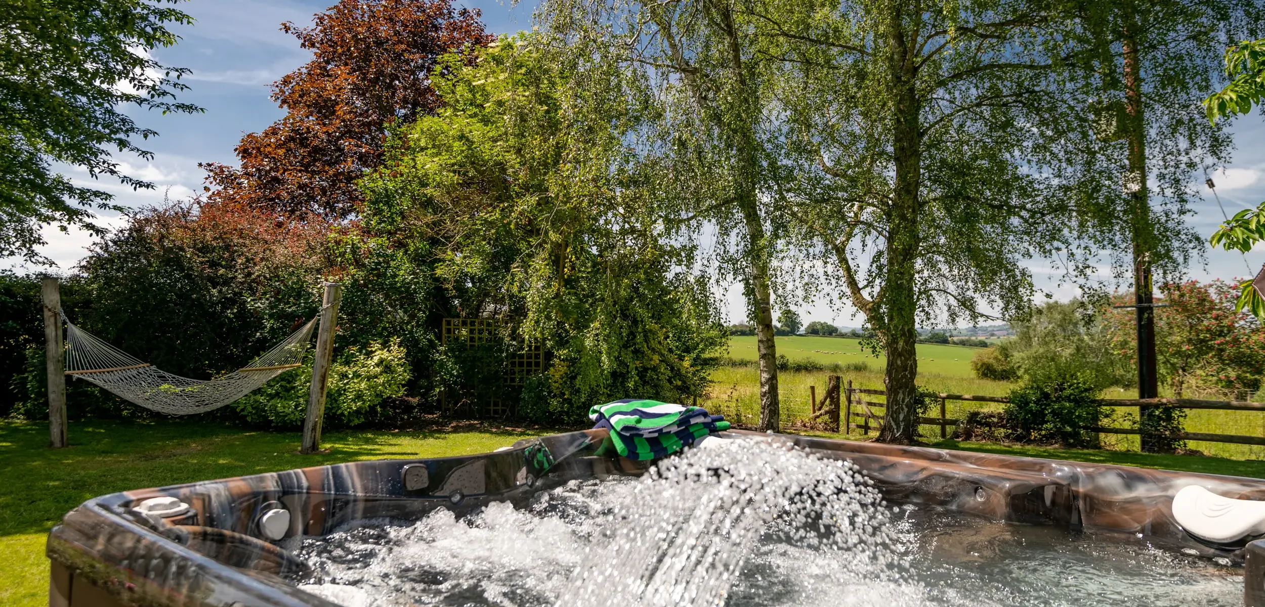 Hot tub in the foreground with garden hammock and countryside views beyond at Old Barn House