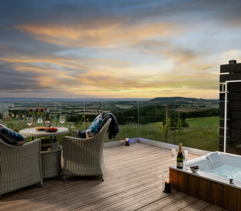 Private decking with double spa bath and outdoor dining overlooking far-reaching countryside views as dusk falls at Peregrine Retreat